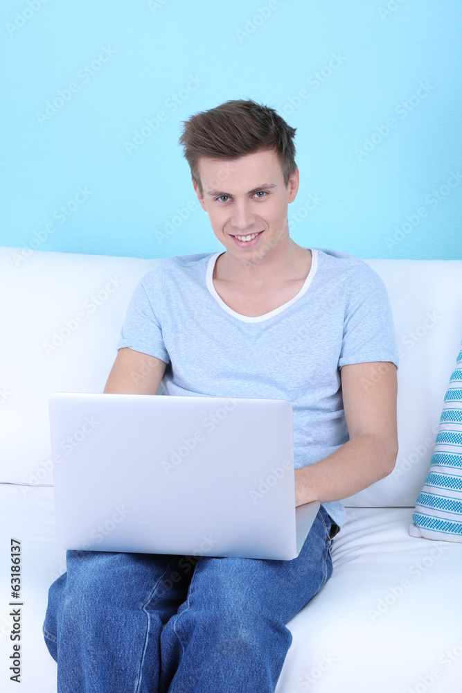 Guy sitting on sofa with laptop on blue background