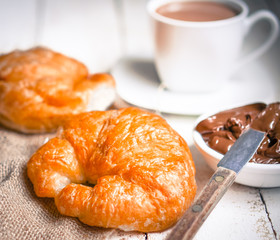 Fresh baked croissants with chocolate cream and hot cocoa on woo