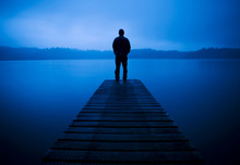 Man Standing On A Jetty By Tranquil Lake