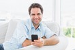 © WavebreakmediaMicro - Smiling man sitting on the couch sending a text