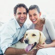 © WavebreakmediaMicro - Happy couple petting their yellow labrador on the couch