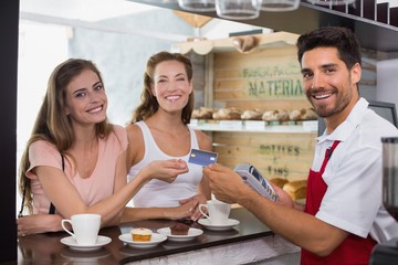 Friends with woman holding out credit card at coffee shop