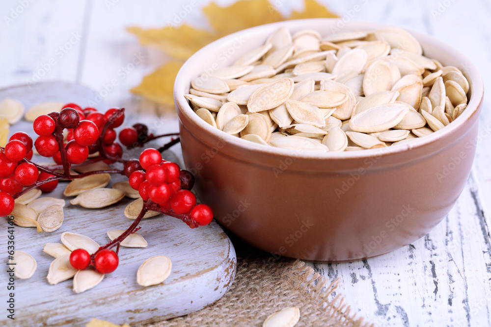 Pumpkin seeds on wooden stand with bowl on table close up