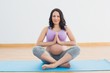 © WavebreakMediaMicro - Pregnant woman sitting on mat in lotus pose smiling at camera