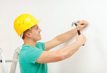 smiling man in helmet hammering nail in wall