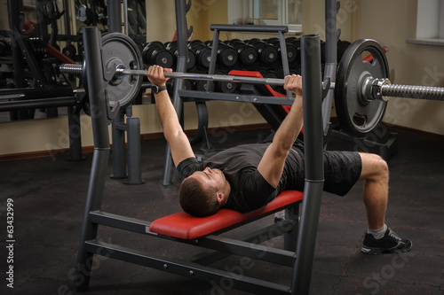 Naklejka na drzwi young man doing bench press workout in gym