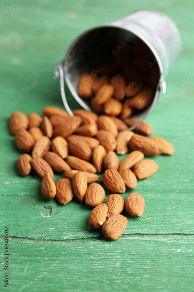 Almonds in bucket on color wooden background