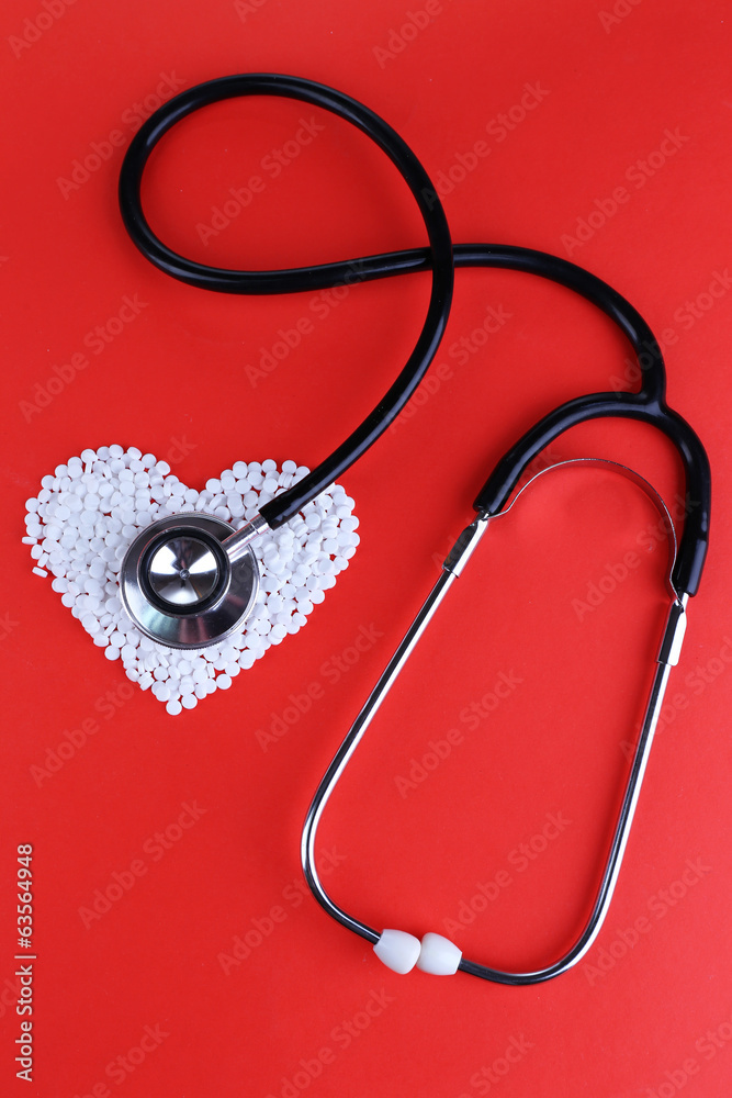 Heart of pills and stethoscope on red background