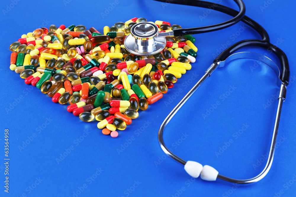 Heart of pills and stethoscope on blue background