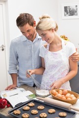 Wall Mural - Couple looking at cook book and preparing cookies in kitchen