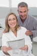 © lightwavemedia - Happy couple in bathrobes reading newspaper in kitchen