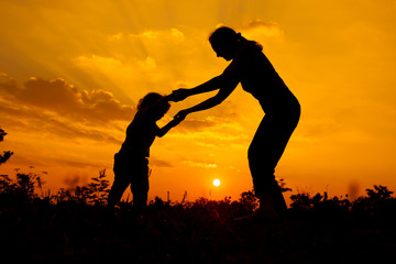 Wall Mural - silhouette of a mother and son who play outdoors at sunset backg