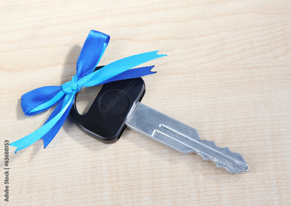 Car key with colorful bow on wooden background
