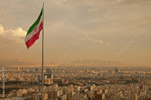 Fotografie, Obraz Iran Flag in the Wind Above Skyline of Tehran
