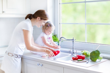 Wall Mural - Young mother and her toddler daughter washing vegetables