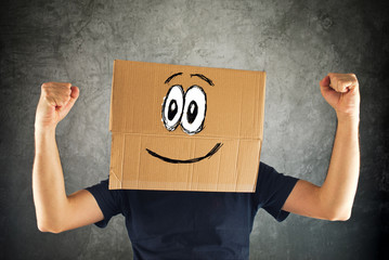 Happy smiling man with cardboard box on his head and raised fist