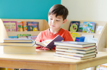 Little boy reading book on table at home