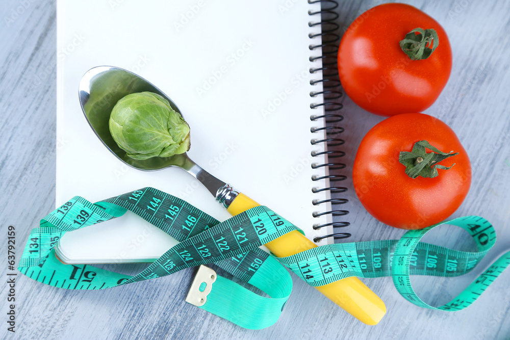 Notebook with measuring tape and vegetables on wooden