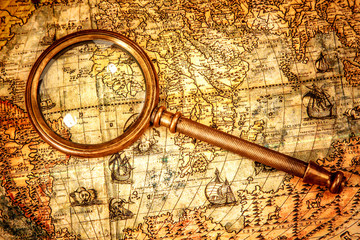 Vintage magnifying glass lies on an ancient world map