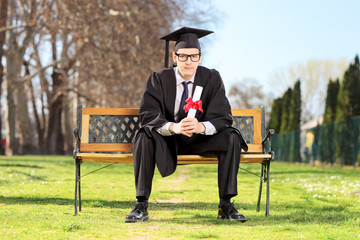 Wall Mural - Male graduate sitting on bench and holding diploma