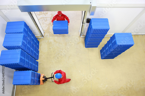 Fotografie, Obraz two workers working with plastic blue boxes in small warehouse