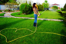 Happy Woman Is Watering Grass In Her Garden