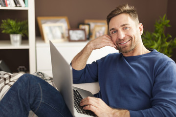 Wall Mural - Portrait of smiling man with laptop on sofa