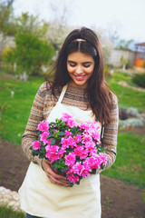 Cute cheerful woman holding flower in pot at garden