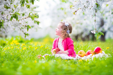 Wall Mural - Cute toddler girl eating apple in spring blooming garden