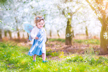 Wall Mural - Cute toddler girl running apple in a blooming garden