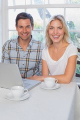 Wall Mural - Portrait of a smiling young couple using laptop in kitchen