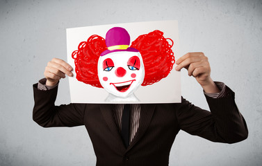 Wall Mural - Businessman holding a cardboard with a clown on it in front of h