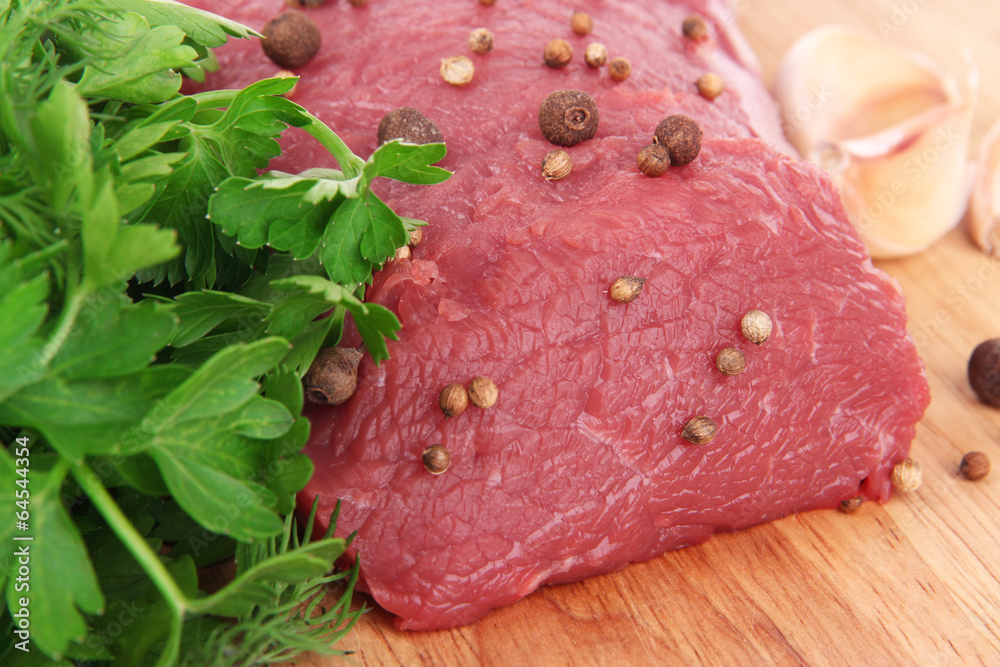 Raw beef meat with spices and greens on wooden background