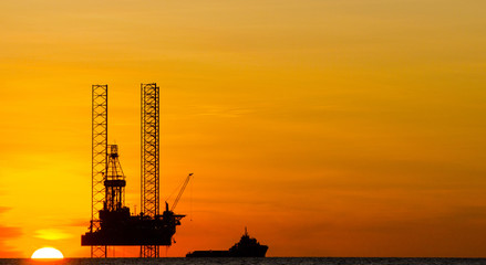 Offshore drilling rig and supply vessel at sunset