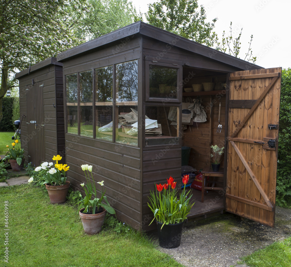 Garden shed with door open, tools, flowers, and plant pots. - obrazy, fototapety, plakaty 