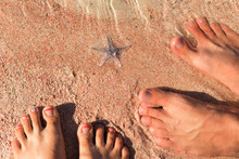 Male And Female Feet Are Standing On Shelly Sand