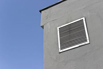 Vent window on gray concrete wall with blue sky