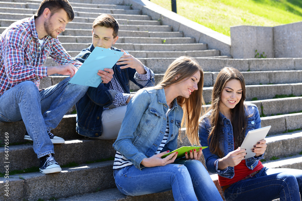 Happy students sitting on stairs in park