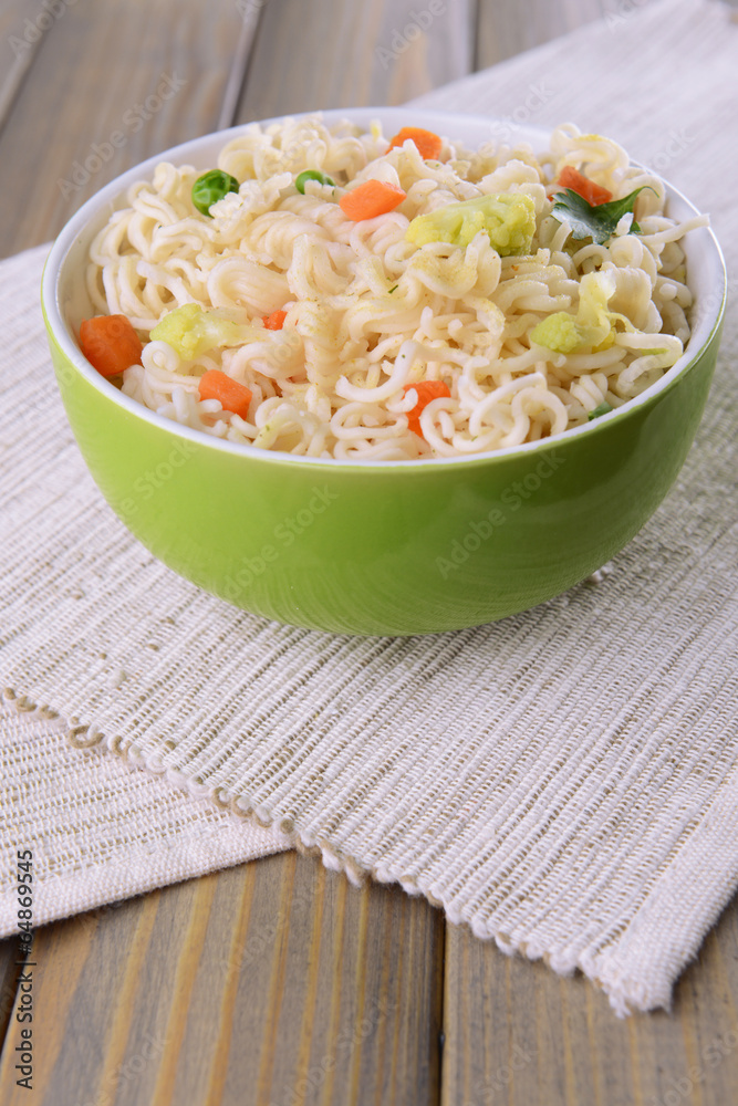 Tasty instant noodles with vegetables in bowl on table close-up