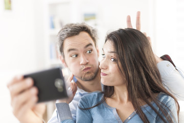 Wall Mural - cheerful couple taking a humoristic selfie with a smartphone