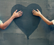 Male And Female Hands Touching Painted Heart On Concrete Wall