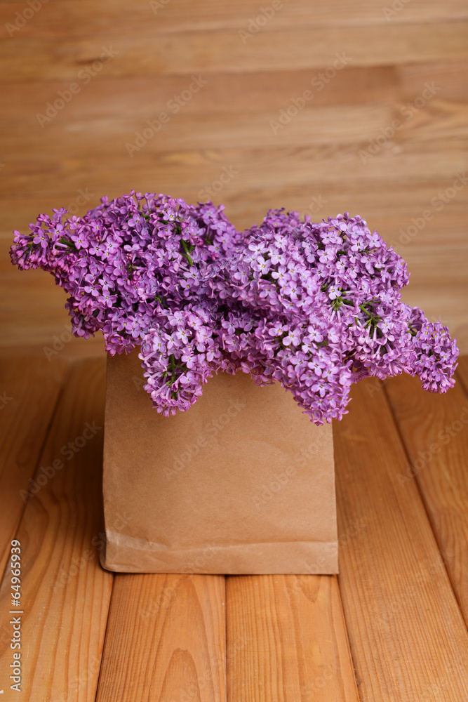 Beautiful lilac flowers in package on table on wooden
