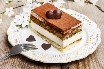 Poster - Tiramisu cake on white plate. Blossom apple branch in the back