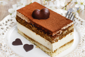 Wall Mural - Tiramisu cake on white plate. Blossom apple branch in the back