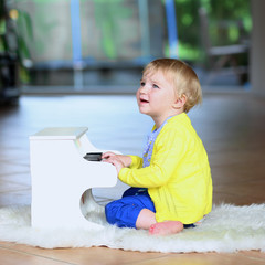 Wall Mural - Happy little girl playing toy piano sitting on the floor