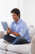 © WavebreakMediaMicro - Happy man sitting on couch using tablet