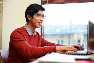 Canvas Print - Smiling asian man in glasses working on laptop in office