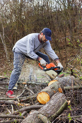 Young man cutting trees using an electrical chainsaw