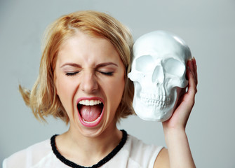 Sticker - Young woman shouting and holding skull on gray background