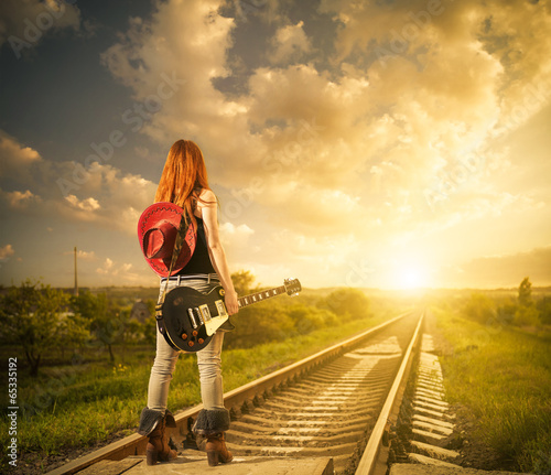 Obraz w ramie redhead woman with guitar at railway distance to sunset